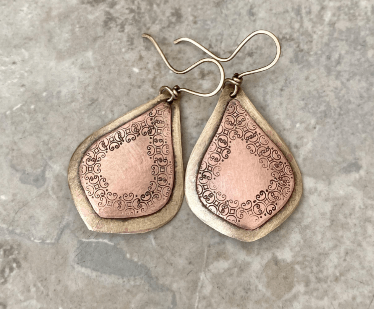 Handmade teardrop earrings with layered copper center and brushed silver backing with etched decorative pattern
