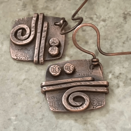 Handmade copper earrings featuring decorative stamped rivets, hammered texture, and wire swirl accents.
