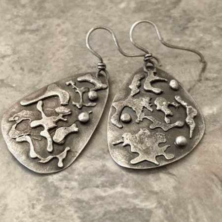 Handmade silver splat earrings featuring organic molten silver shapes soldered onto teardrop-shaped metal earrings.